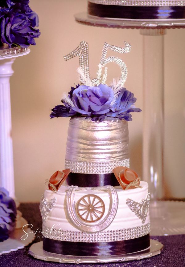 Elegant 15th birthday cake with silver, purple flowers, and cowboy hat decorations.
