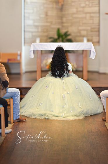 A girl in a ball gown kneeling at an altar in a church.