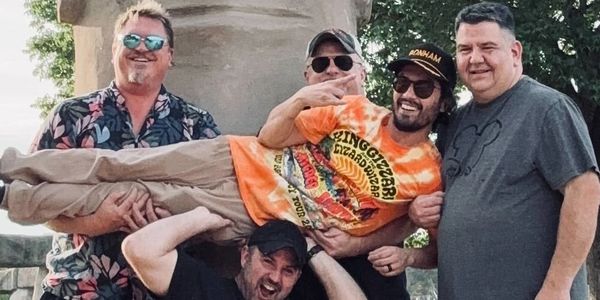 Five men posing with one man playfully held horizontally.