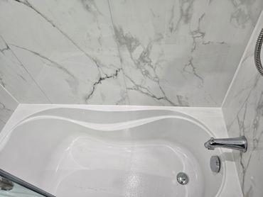 Smooth white caulking bead sealing the joint between a bathtub and marble-look wall panels