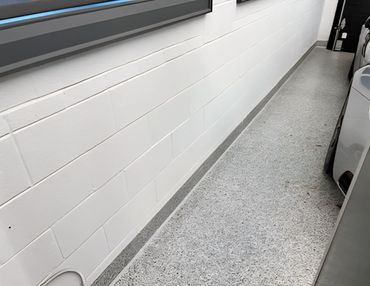 Neatly applied grey caulk line sealing the gap between a paneled wall and garage floor.