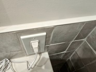 Fine caulk line sealing the transition between tiled backsplash and painted wall near an outlet.