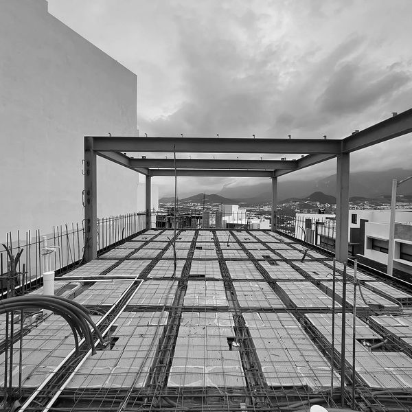 Black and white image of a rooftop under construction with metal framework and cloudy sky.