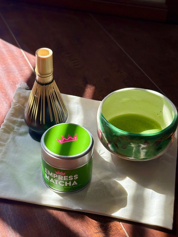 Ceremonial matcha set with whisk, tin, and bowl on a cloth.