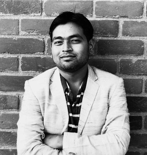 Confident man in a light blazer poses against a brick wall.