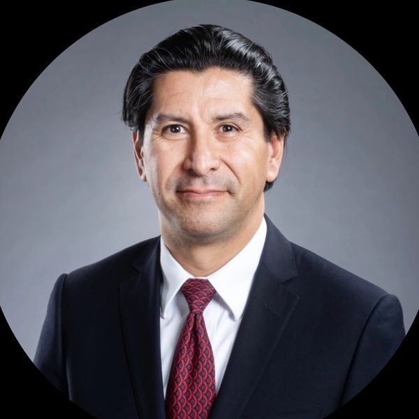 Professional headshot of a man in a suit and red patterned tie.