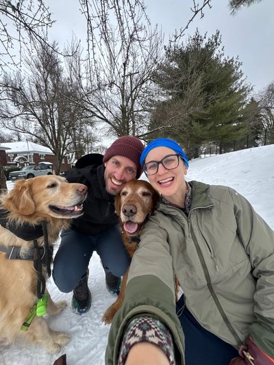Happy couple with two dogs enjoying a snowy day outdoors.