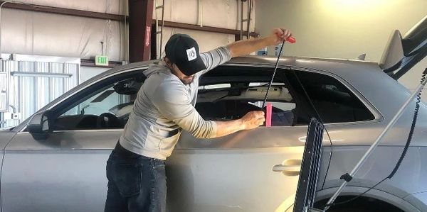 A man repairs a car door using a tool in a garage.