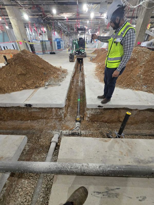 Worker inspecting underground piping inside a construction site.