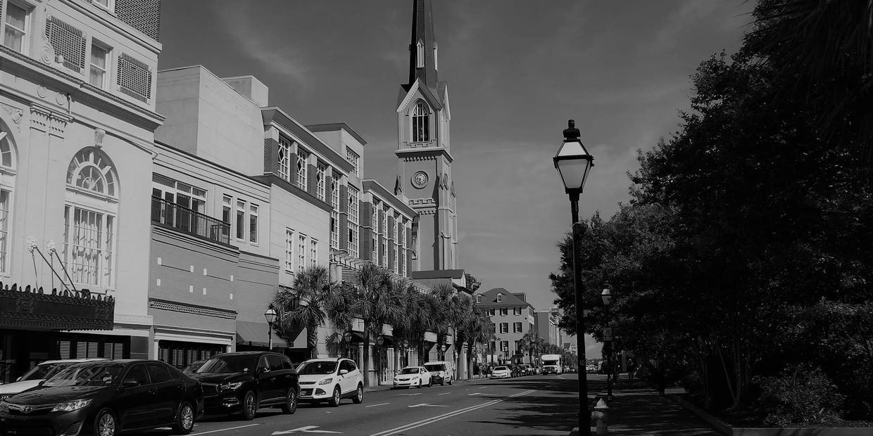 Historic street with cars, palm trees, and a tall church steeple in the background.