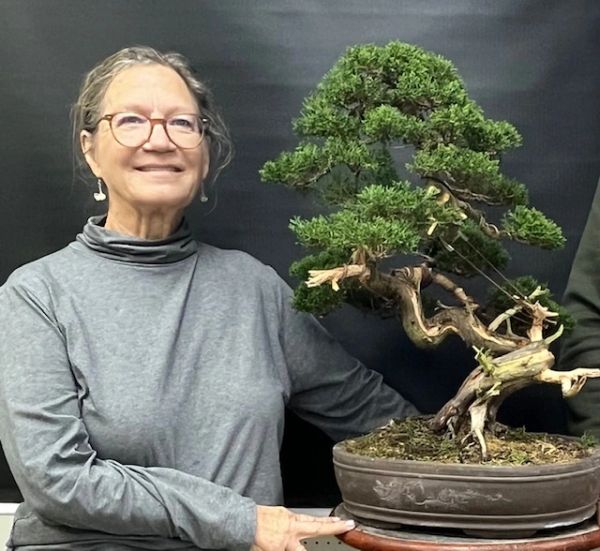 Woman posing with a large bonsai tree in a decorative pot.