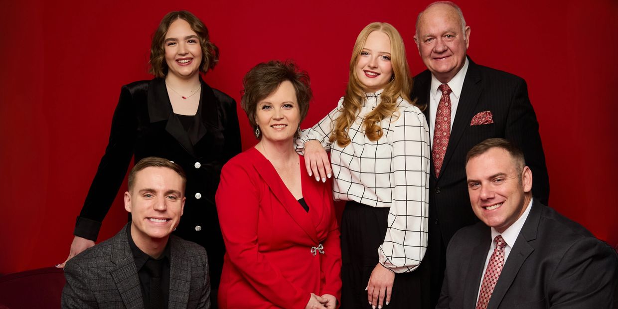 A smiling multi-generation family portrait in formal attire against a red backdrop.