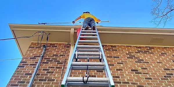 employee on a ladder with ladder stabilizer cleaning gutters with an extension pole