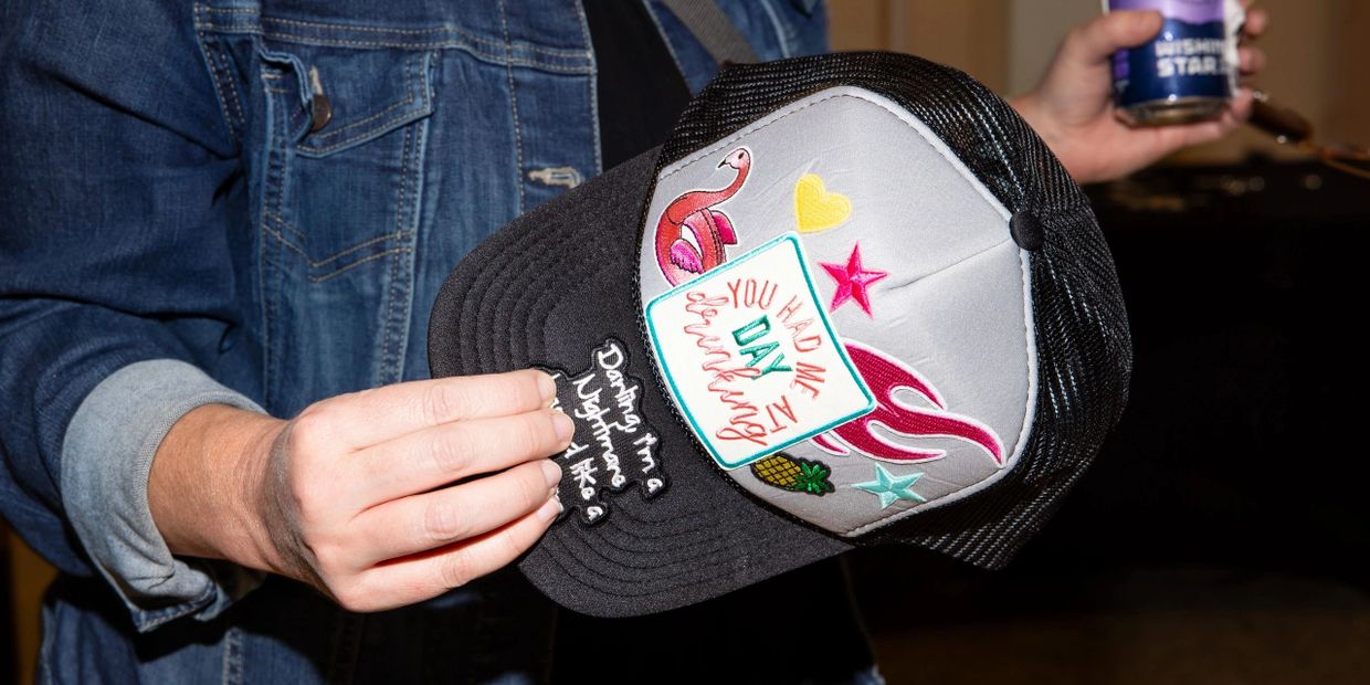 Person holding a colorful embroidered cap with various patches and text.