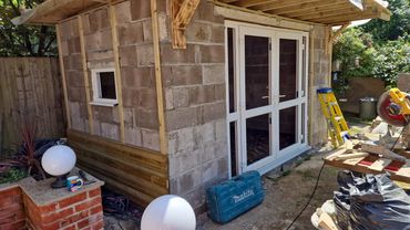 Under construction garden shed with tools and materials nearby.