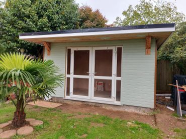 A small garden shed with white double doors and greenery.