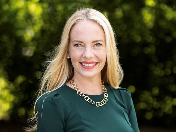 Woman standing and smiling outside wearing green and a gold necklace.
