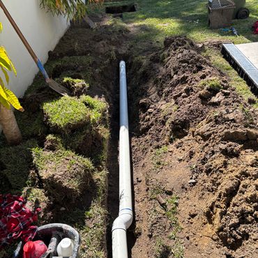 PVC pipe being installed in a dug trench in a backyard.