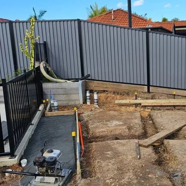 Construction site preparing foundation with pipes and wooden planks in a fenced backyard.