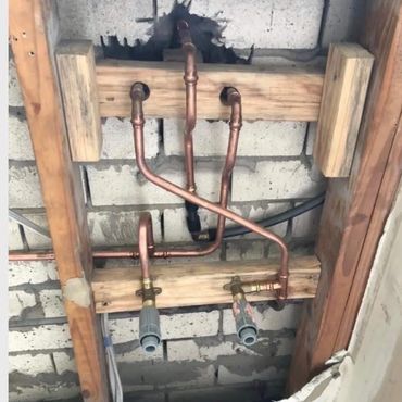 Copper plumbing pipes installed within a wooden frame against a brick wall.