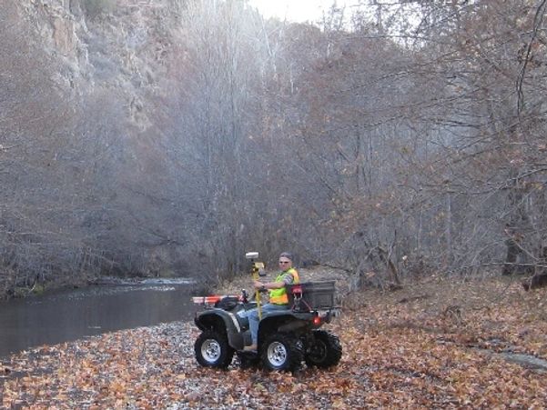 Person on an ATV near a river in a leaf-covered forest.