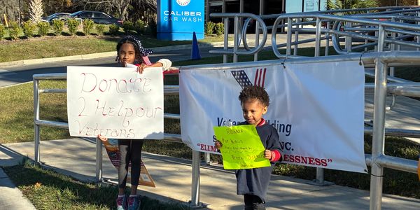 Two children holding signs asking for donations to help veterans.