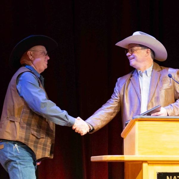 Two men in cowboy hats shaking hands on stage.