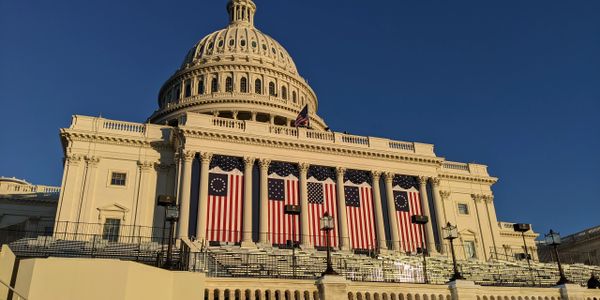 The U.S. Capitol building adorned with patriotic flags and bunting in bright sunlight.