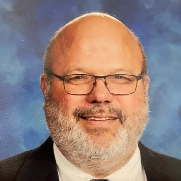 Smiling bald man with glasses and beard in formal attire.