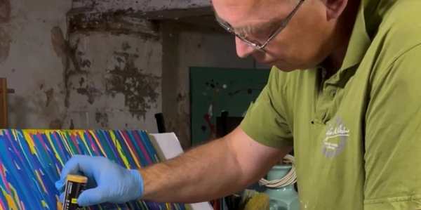 The image shows the abstract artist called Angus Fraser applying paint by hand to a canvass