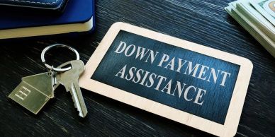A chalkboard sign reading "DOWN PAYMENT ASSISTANCE" beside house keys.