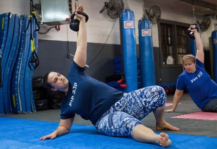 Woman lifts kettlebell above her head while leaning on the ground.