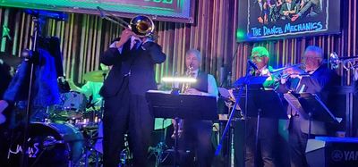 A live jazz band performing at The Warehouse with vibrant blue and green lighting.