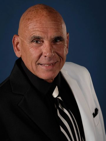 Smiling bald man in a stylish black and white suit with a striped tie.