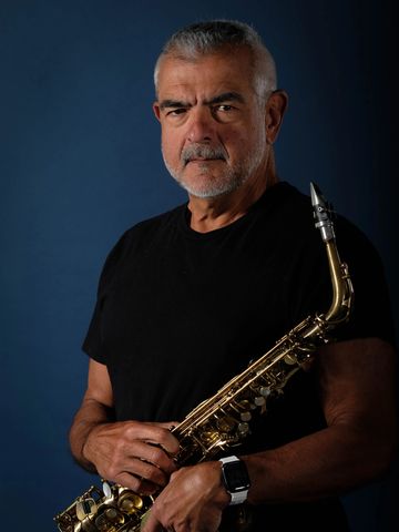 Mature man holding a saxophone against a dark blue background.