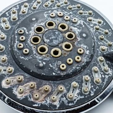 Close-up of mineral scale buildup on a showerhead caused by hard water, showing the effects of calci