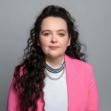 Professional portrait of a woman with curly dark hair wearing a pink blazer.