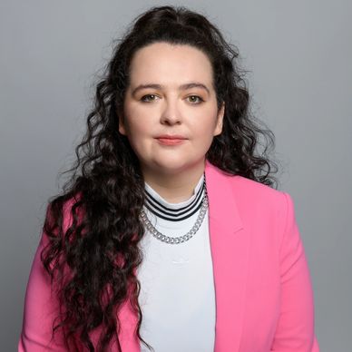 Professional portrait of a woman with curly dark hair wearing a pink blazer.