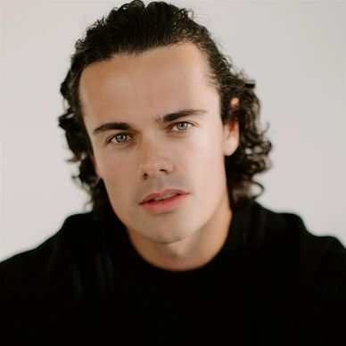 Close-up of a young man with curly hair and green eyes.