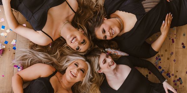 Four women in black dresses lying on the floor smiling.