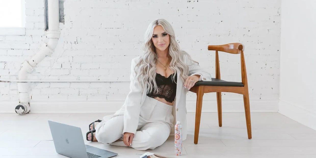 Woman in white suit sitting on floor next to chair and laptop.