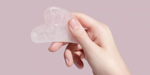 Hand holding a heart-shaped clear crystal against a soft pink background.