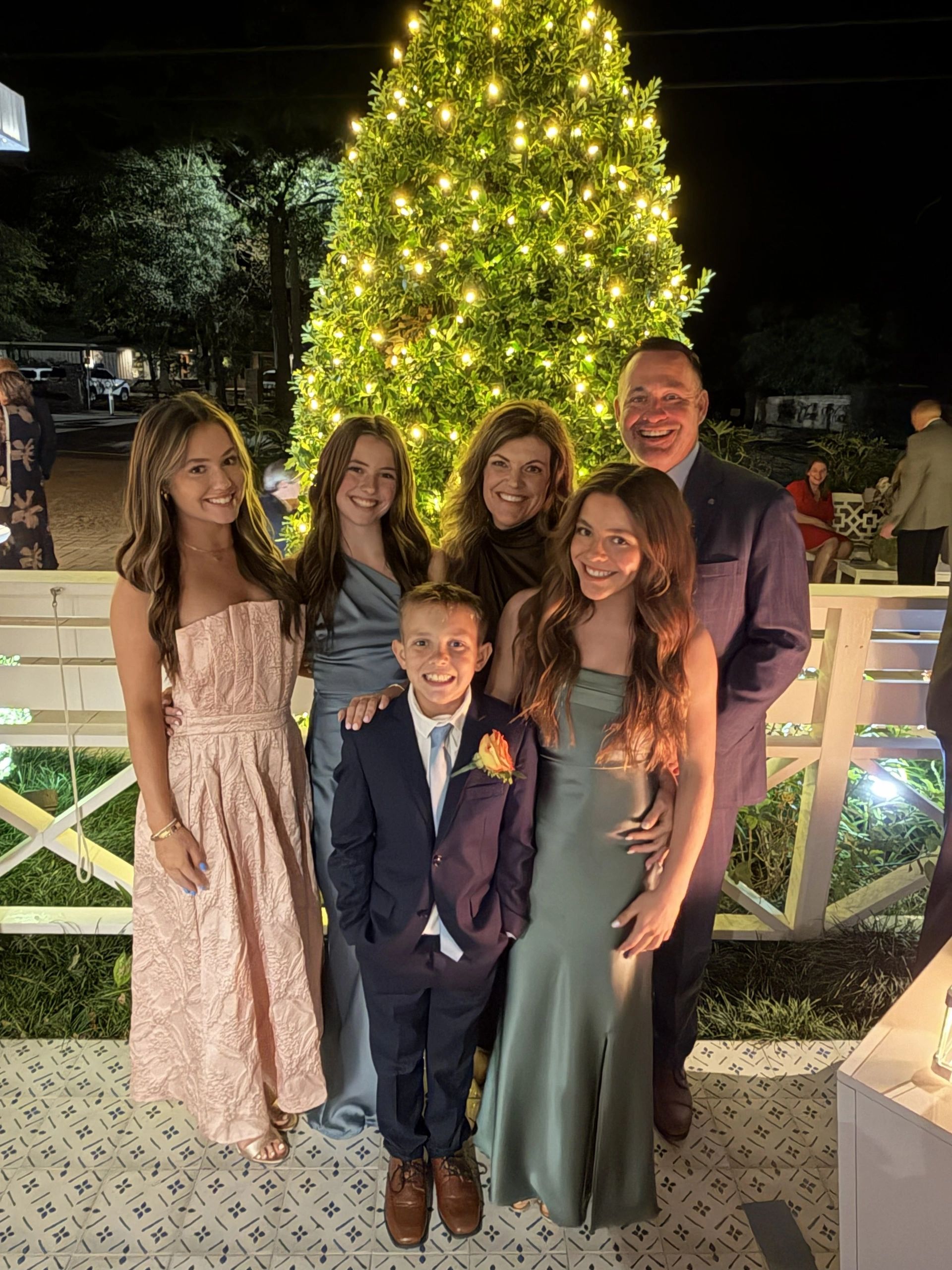 A family posing joyfully in front of a lit-up tree at night.