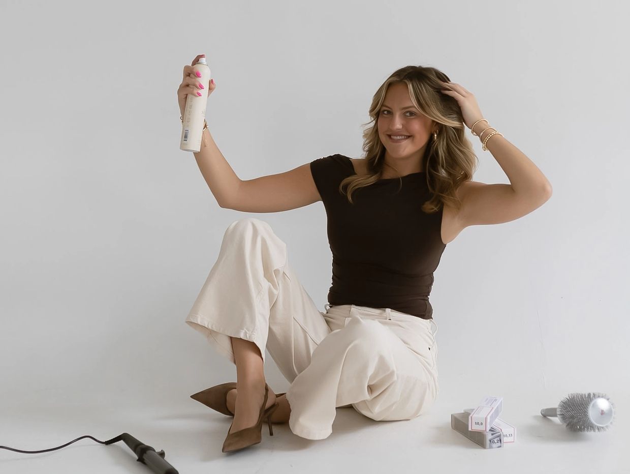 Smiling woman holding a spray can, sitting on the floor in a casual outfit.