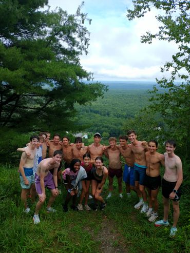 Group of teenagers posing shirtless on a hilltop with a forest view.