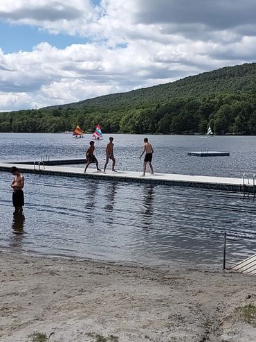 Boys enjoying a sunny day on a lake dock with sailboats in the background.