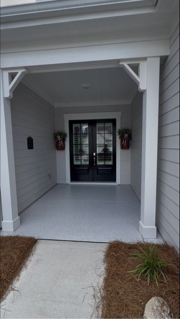 Modern front porch with black double doors and potted plants.