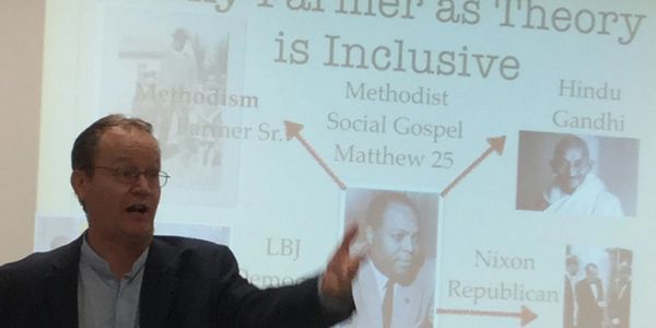 Speaker presenting a slide on the inclusiveness of Farmer as Theory with historical figures.