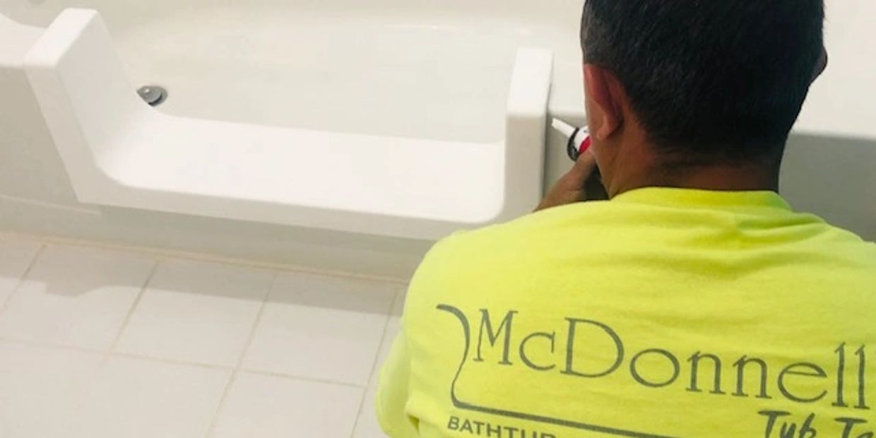 Worker refinishing a bathtub in a bathroom.