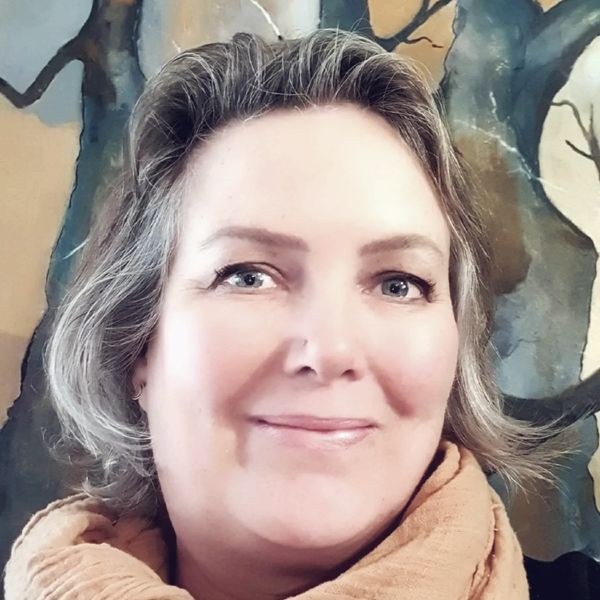 Smiling woman with gray hair and beige scarf in front of a tree mural.